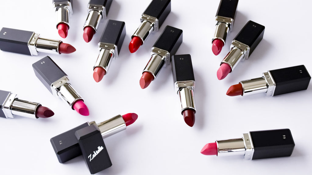 Zakiella clean lipsticks made with natural and organic ingredients shown in a wide inclusive shade range with tubes open and a lipstick cap showing the logo